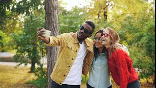 Cheerful friends multiracial group are taking selfie wearing sunglasses and hugging standing in park [upl. by Ymirej]